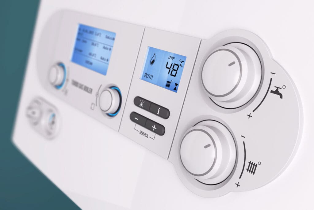 Close-up of a modern boiler control panel with two digital displays and several round control knobs. The screens show temperature, symbols, and mode settings. The panel is mostly white with gray and blue details.